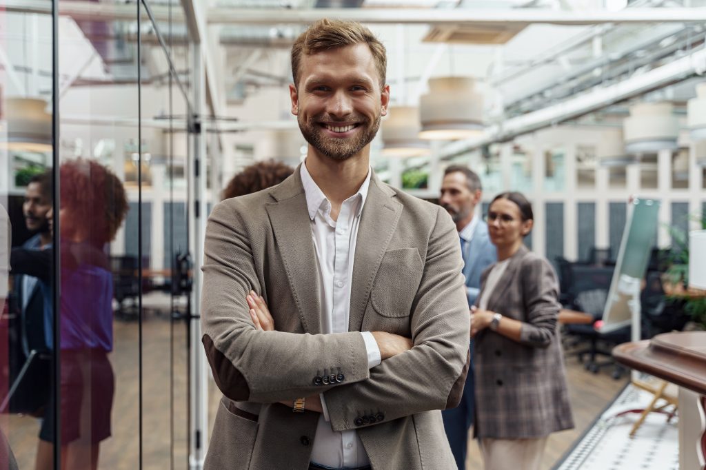 Portrait of smiling businessman standing in modern office on colleagues background